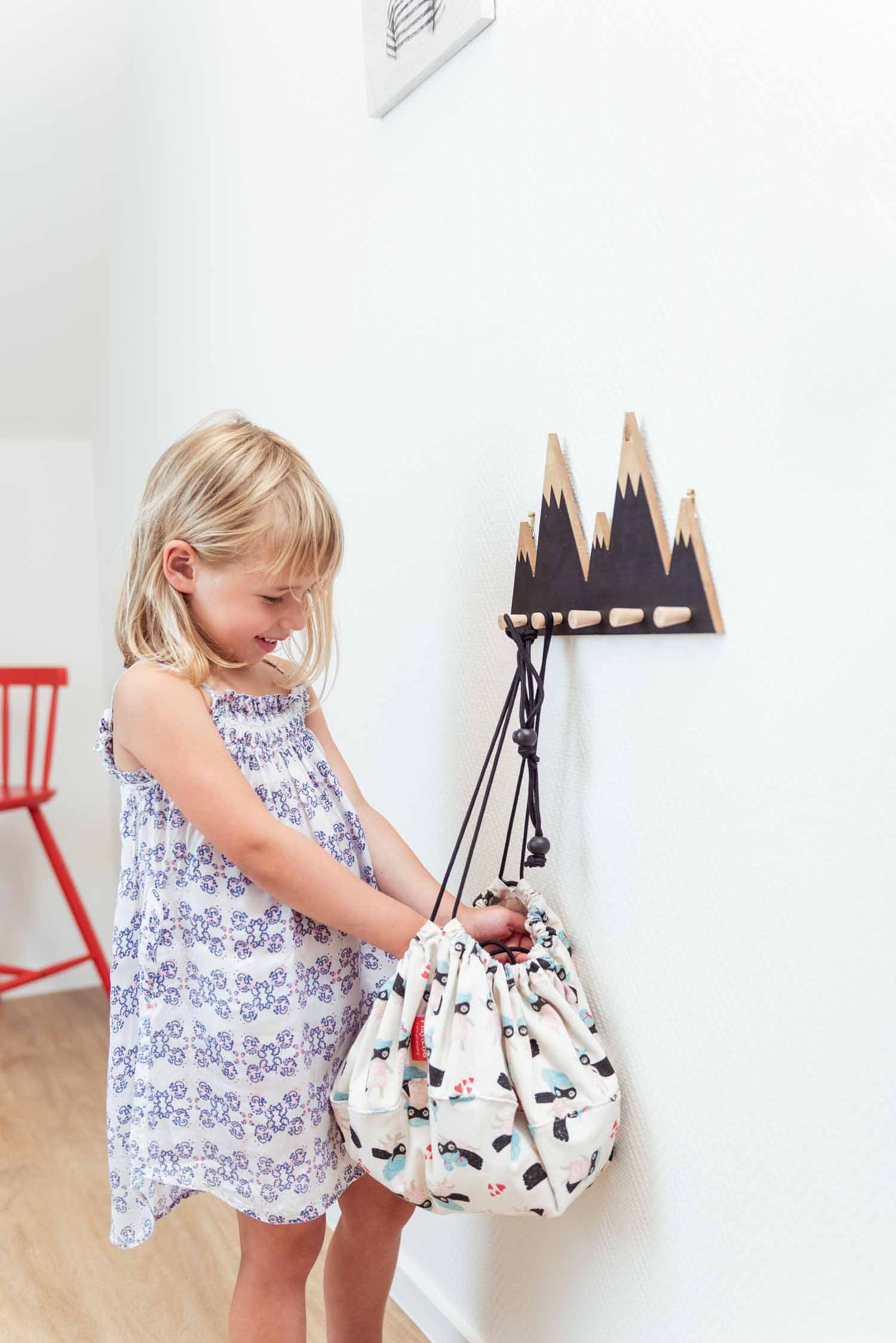 supergirl mini toy storage bag, bag hanging on coat rack, girl taking something out of the bag