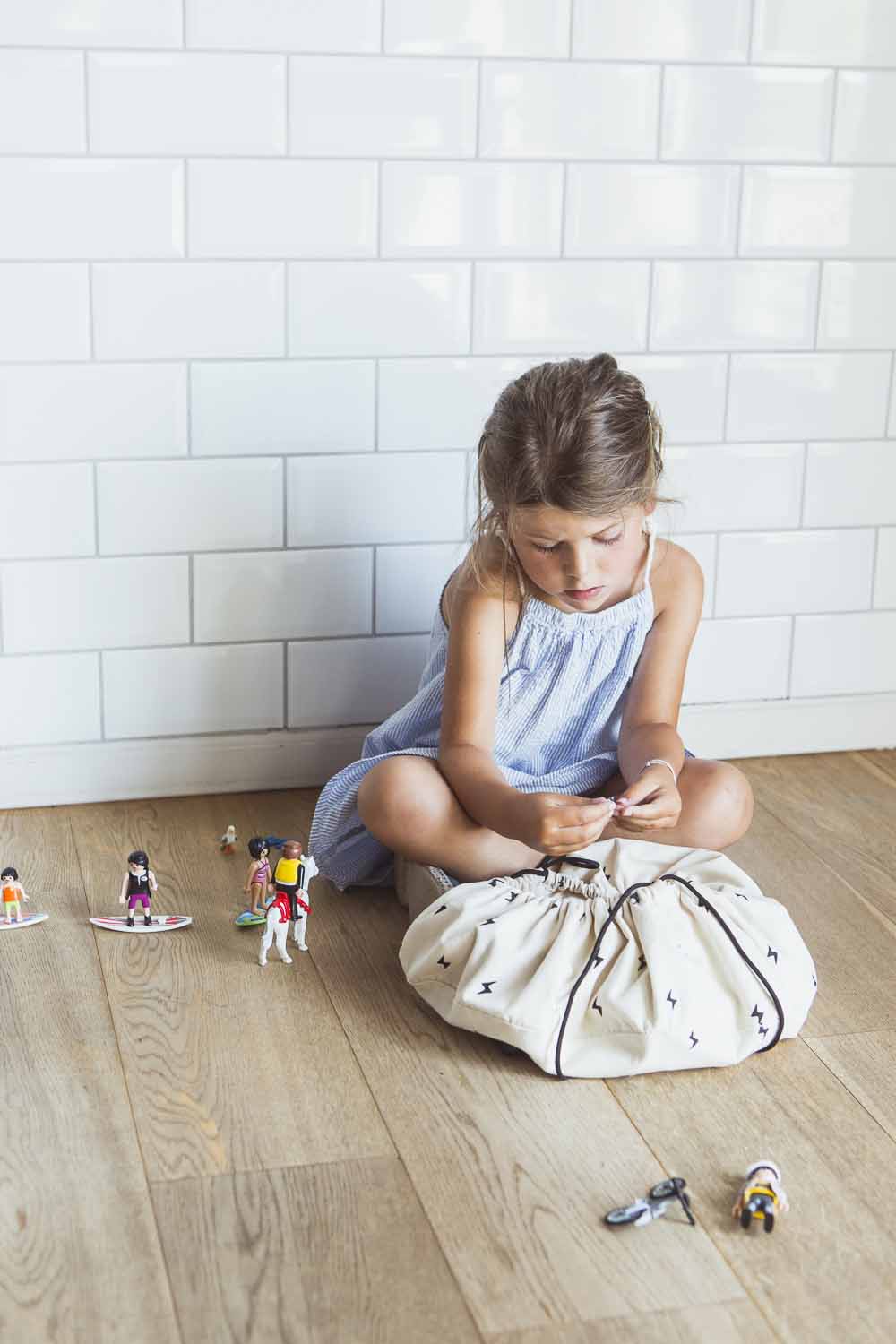 thunderstrike mini toy storage bag, bag on floor, playing girl sitting on floor next to bag and toys