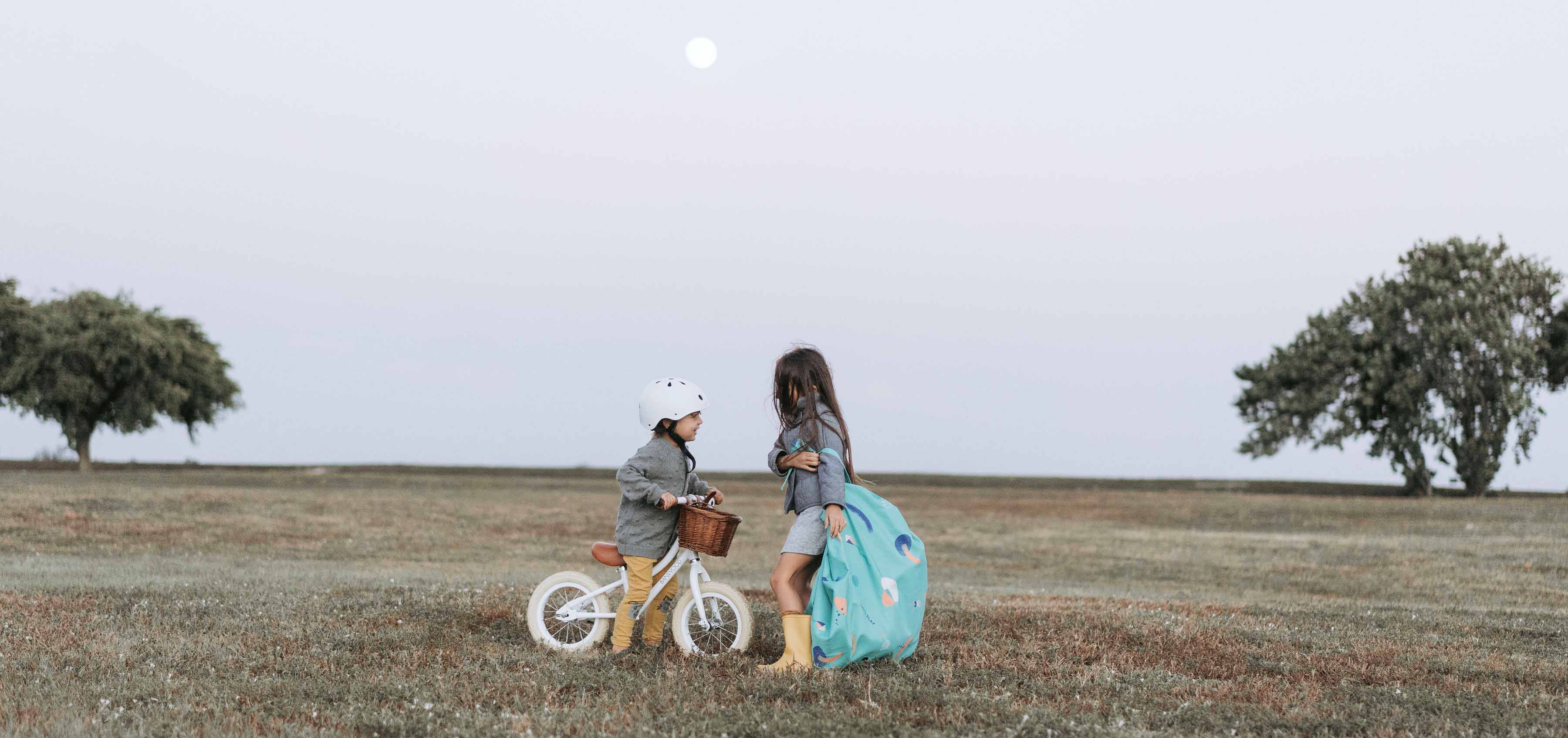 outdoor play storage bag, girl carrying the bag, other child on bicycle