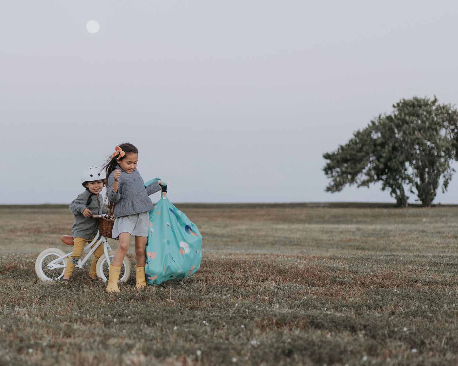 outdoor play storage bag, girl carrying the bag, other child on bicycle