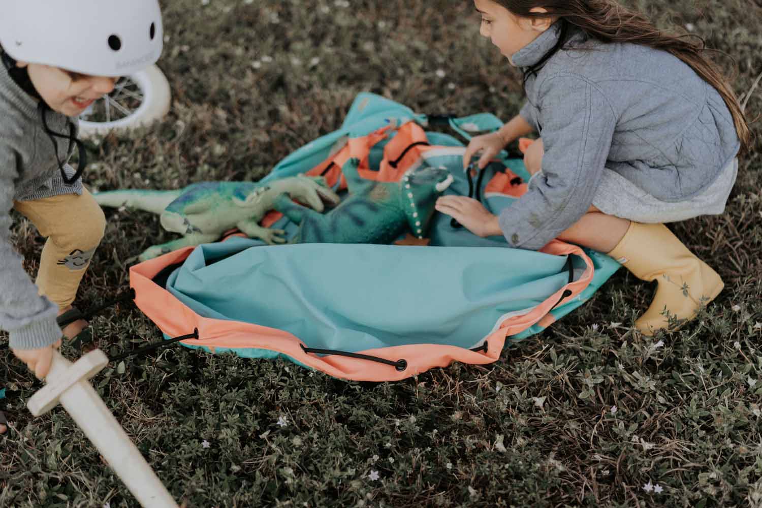 outdoor play storage bag, 2 kids playing with dinos on the mat in a field