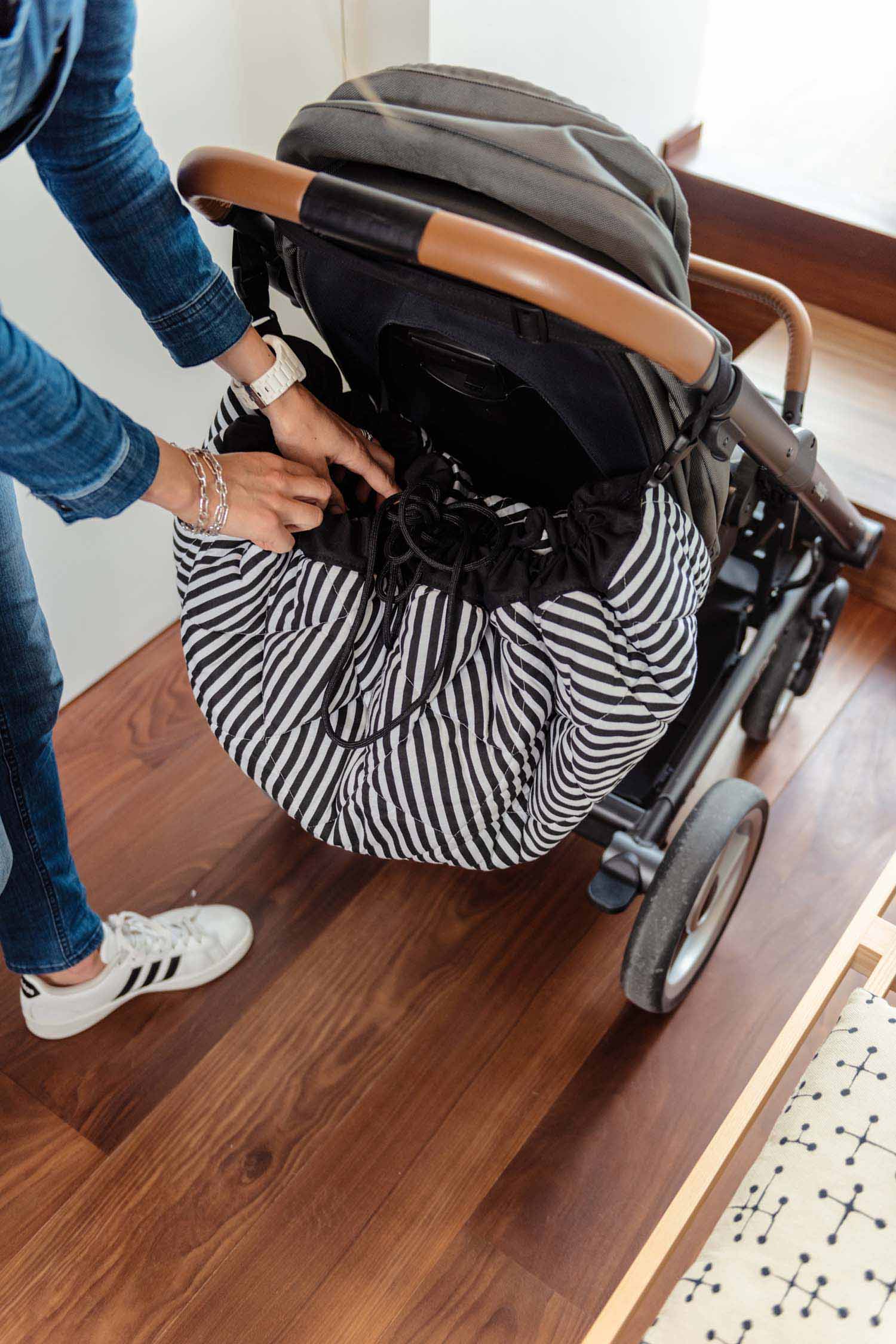Play&Go storage bag and soft padded baby mat, woman taking out something out of black and white striped bag, hanging on pram