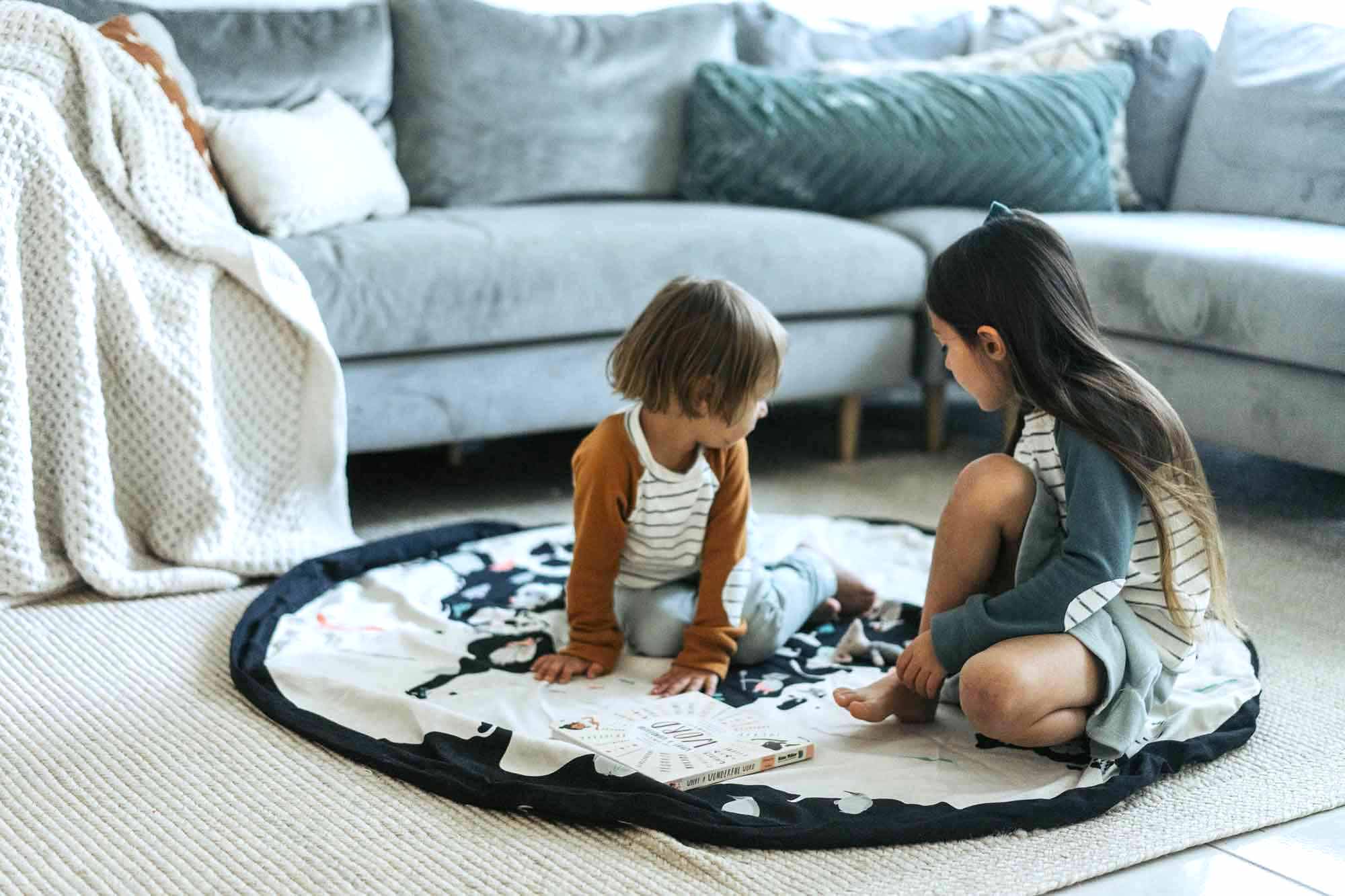 worldmap/stars toy storage bag, 2 playing kids on mat in living room, next to sofa