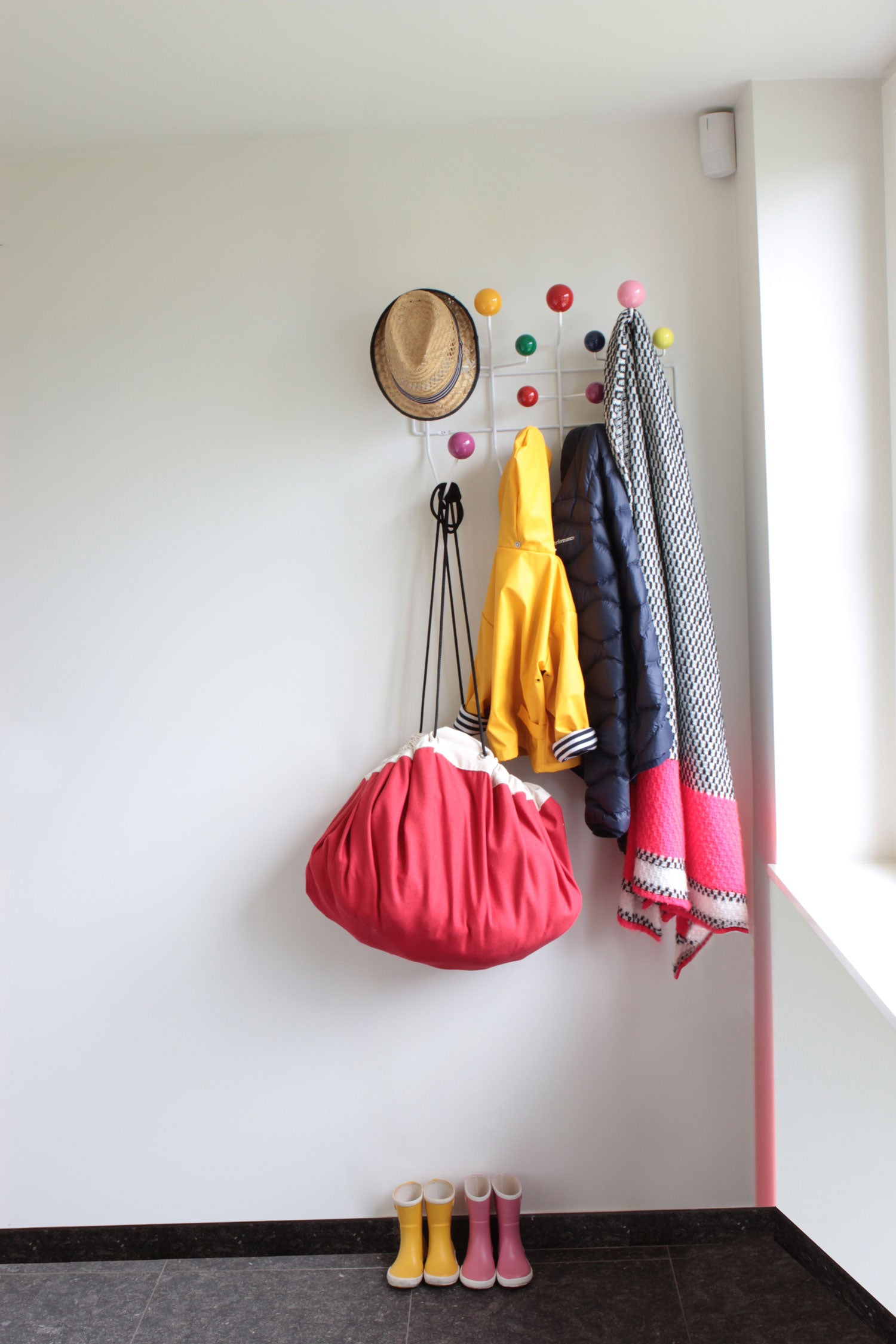 Play&Go storage bag, red bag hanging on coat rack, lots of jackets and shoes