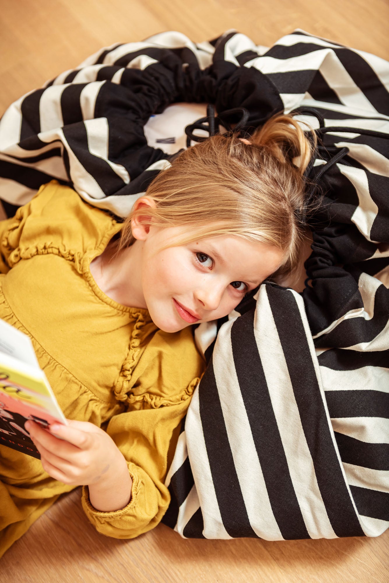 toy storage bag and play mat, black and white stripes, girl lying on mat reading a book
