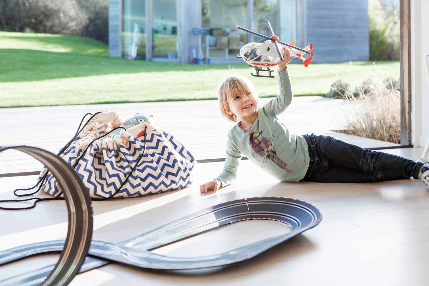 zig zag blue toy storage bag, filled with toys, playing kid with heli, bag filled with toys on floor